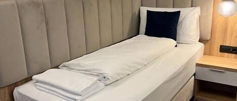 A modern bedroom with a wooden panel wall, a padded headboard, a bedside table with a lamp, and a neatly made bed.