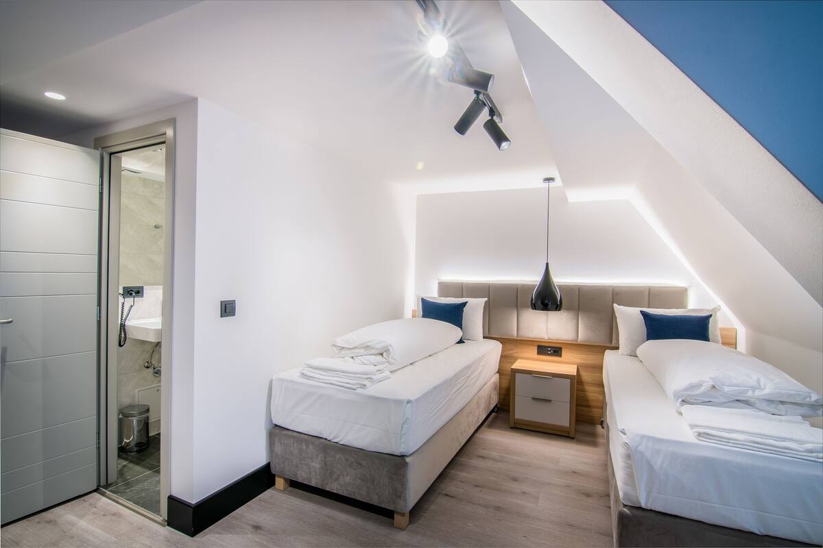 Un dormitorio moderno con dos camas, una mesita de noche y una lámpara de techo.