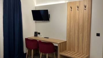 Een moderne slaapkamer met een bed, een bureau met twee stoelen, een televisie en een kledingkast.