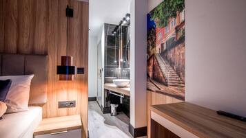 A modern hotel room with a wooden headboard, a bedside table, a nightstand, a large window, and a painting of a cityscape.
