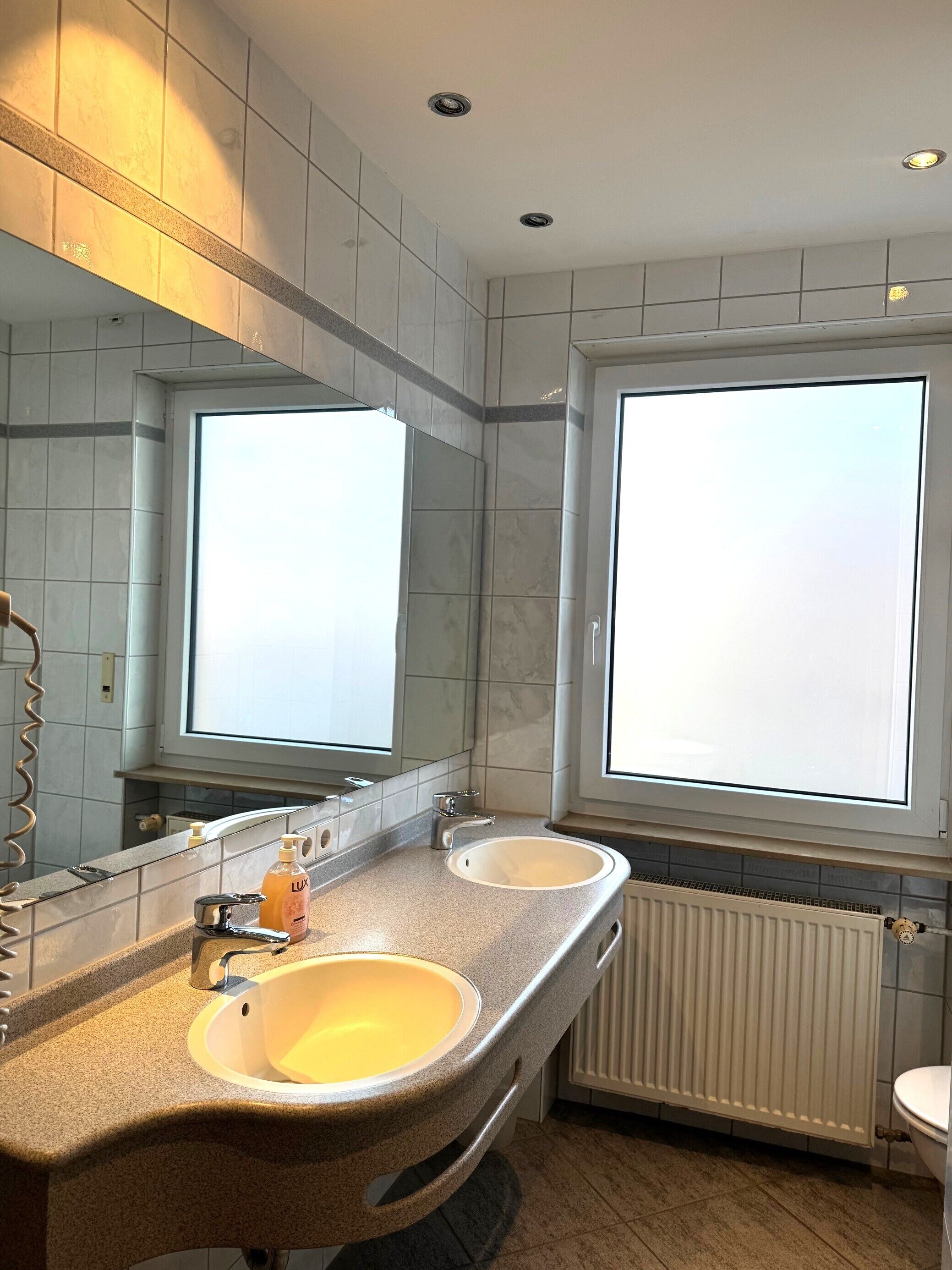 Ein modernes Badezimmer mit zwei Waschbecken, einem großen Spiegel und einem Fenster für natürliches Licht.