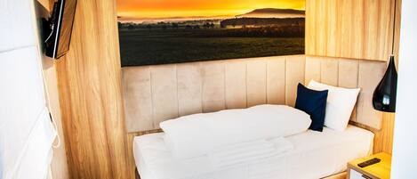 Una cama bien hecha con sábanas blancas, un cabecero de madera y un control remoto sobre una mesita de noche de madera.