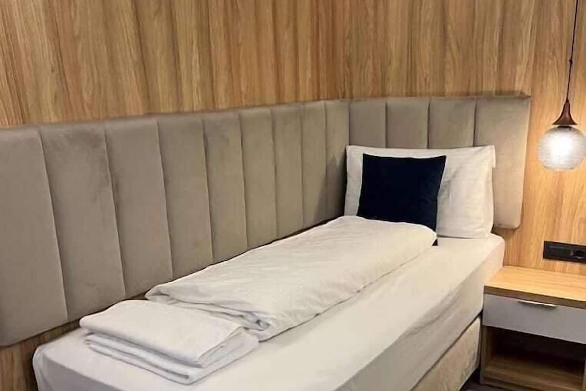 Una cama individual con cabecera, una mesita de noche y una lámpara colgante en una habitación con paneles de madera.