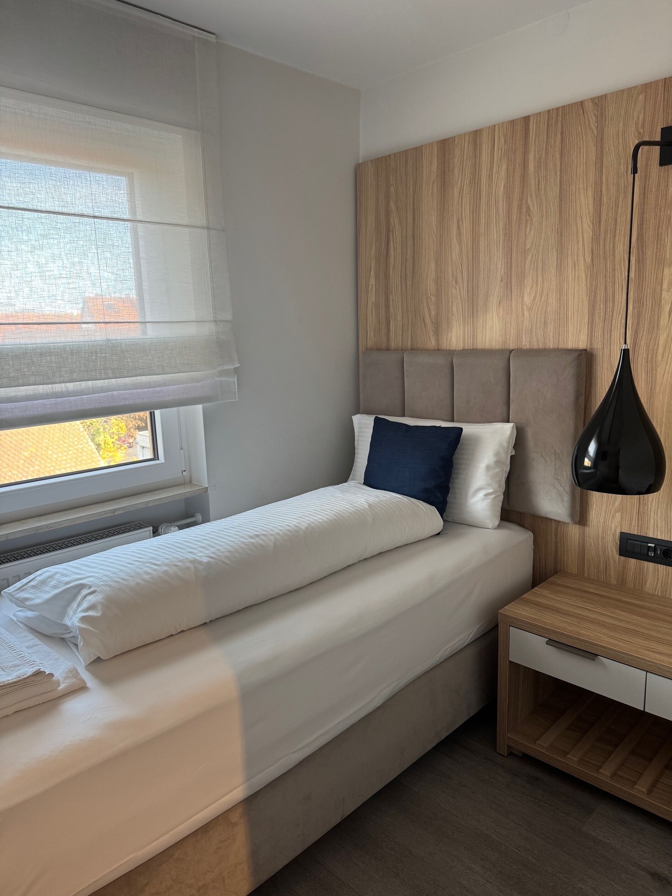 A modern bedroom with a bed, bedside table, and a window with blinds.