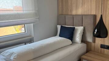 A modern bedroom with a bed, bedside table, and a window with blinds.