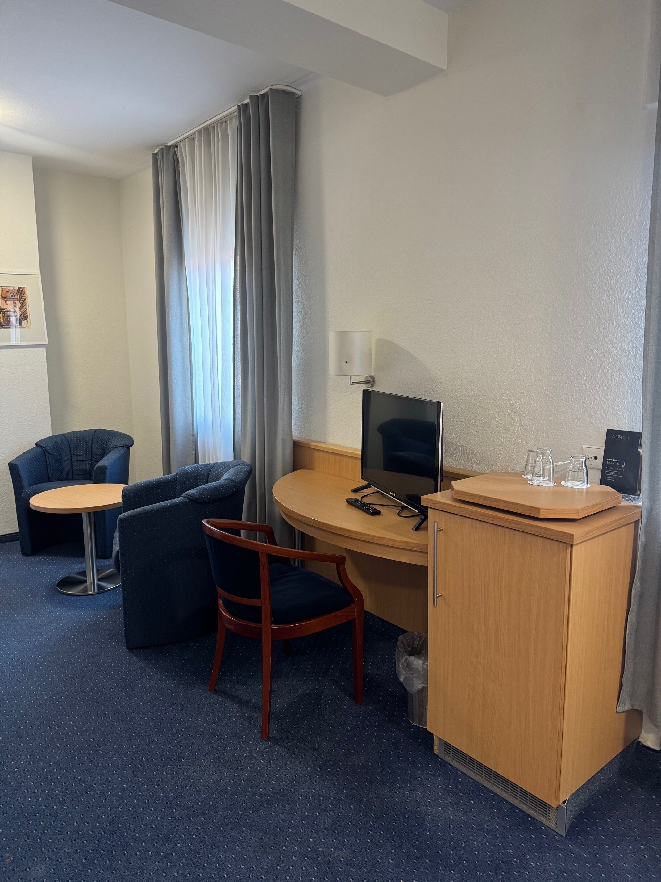 Habitación de hotel con escritorio, dos sillas, una mesita, televisor y minibar.
