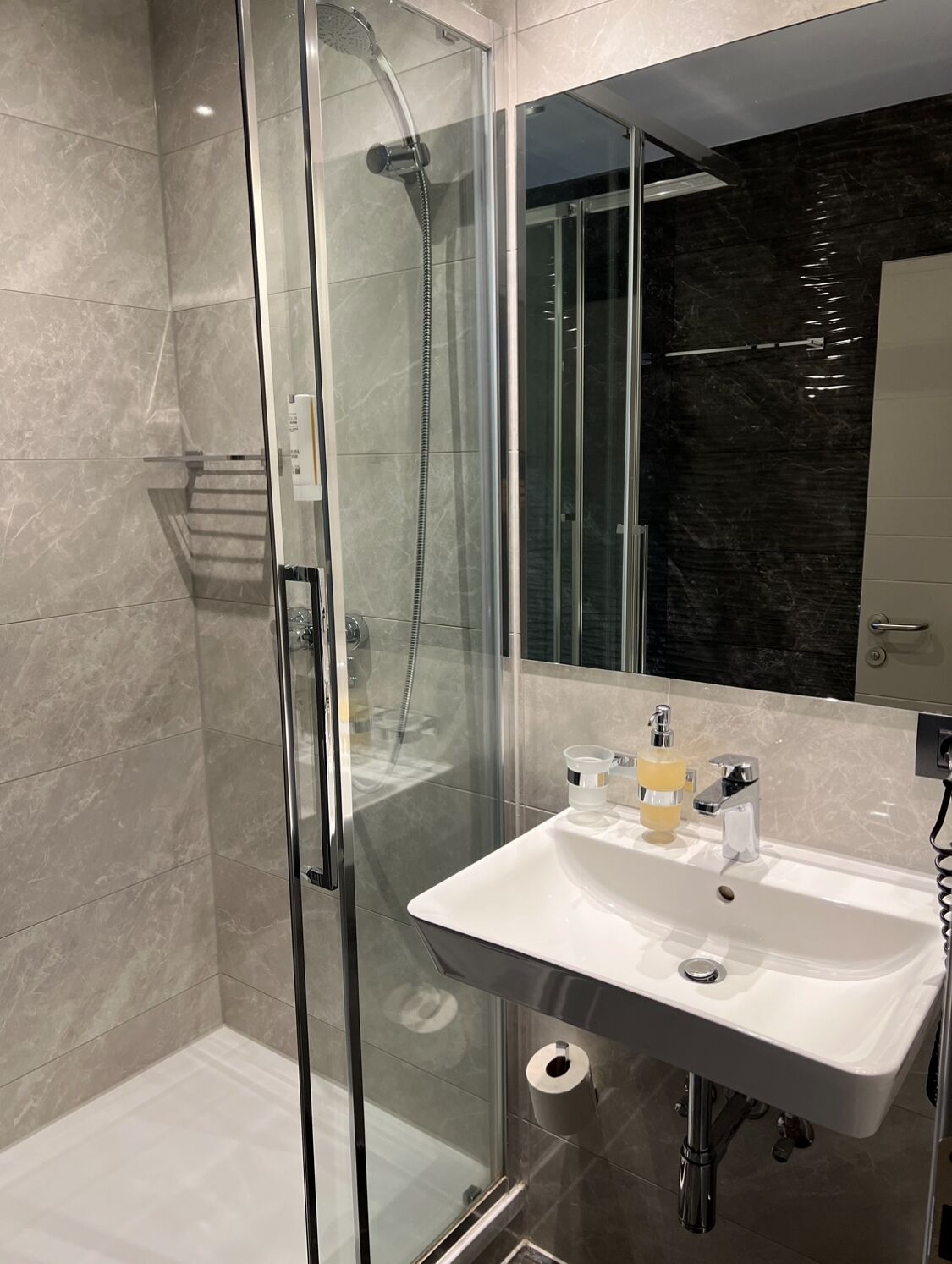 Ein modernes Badezimmer mit einer in Glas eingefassten Dusche, einem weißen Waschbecken und einer dunklen Marmor-Spritzschutzwand.