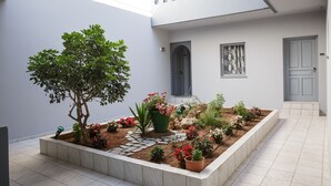 Un patio con un árbol, plantas en macetas y piso de baldosas.