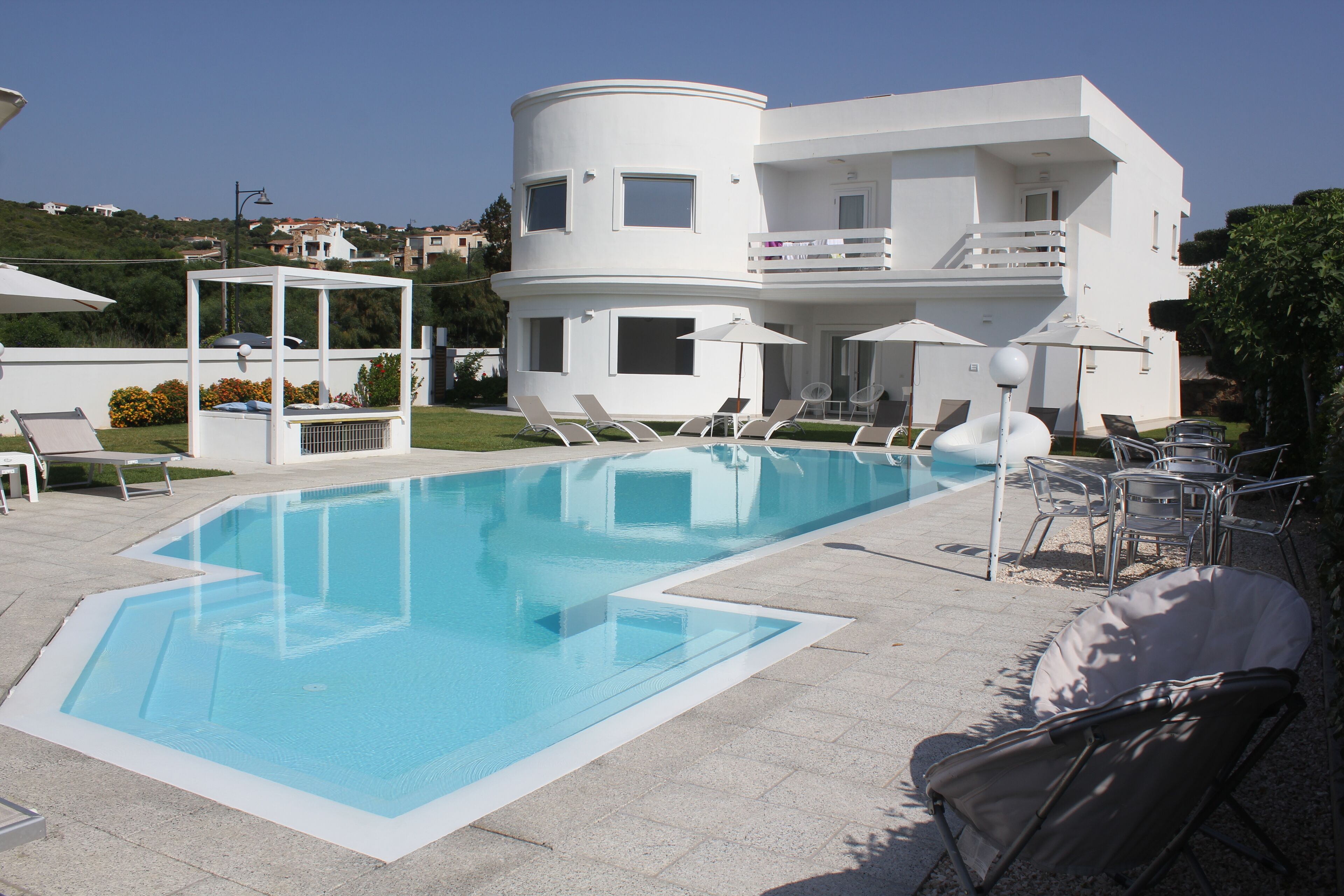 Un bâtiment moderne de couleur blanche, doté d’une piscine, de chaises longues et de parasols.