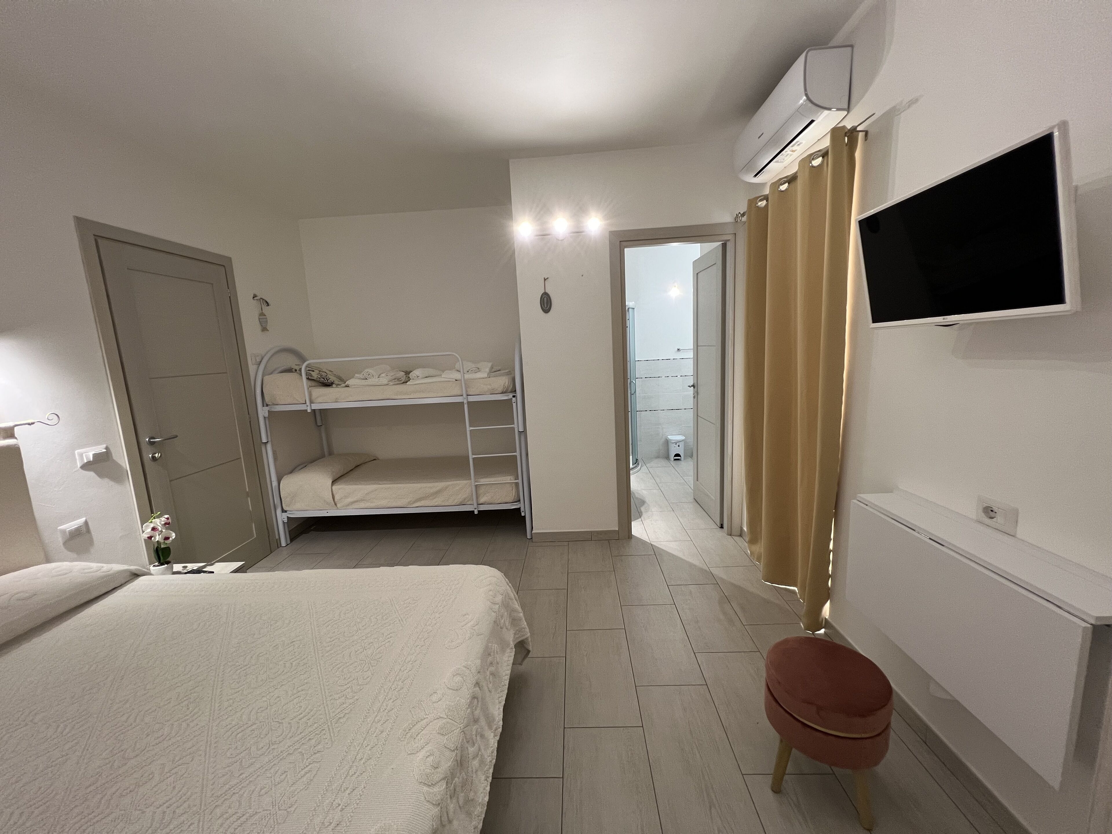 Ein Schlafzimmer mit Etagenbett, Einzelbett, Wandfernseher und kleinem Schreibtisch.