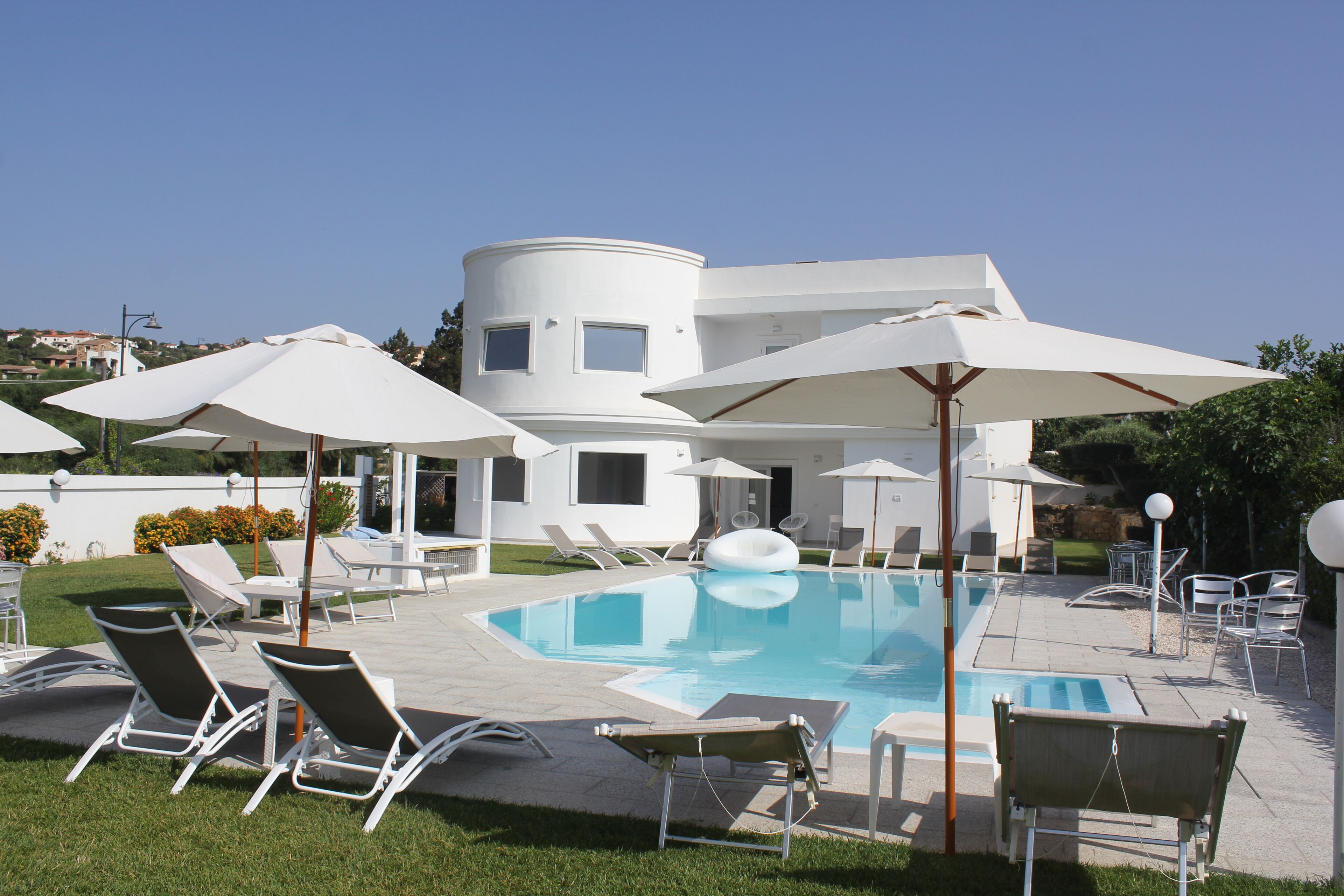 A modern pool area with lounge chairs and umbrellas, a clear blue pool, and a white building with multiple windows.