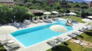 A swimming pool with lounge chairs and umbrellas, surrounded by greenery and buildings in the background. - Al Mare da Francesca (Olbia)