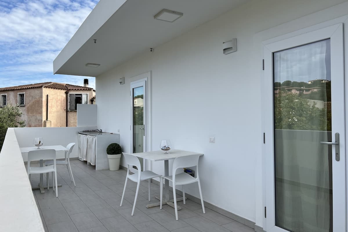 A balcony with white furniture, including two tables and four chairs, a potted plant, and a sliding glass door.