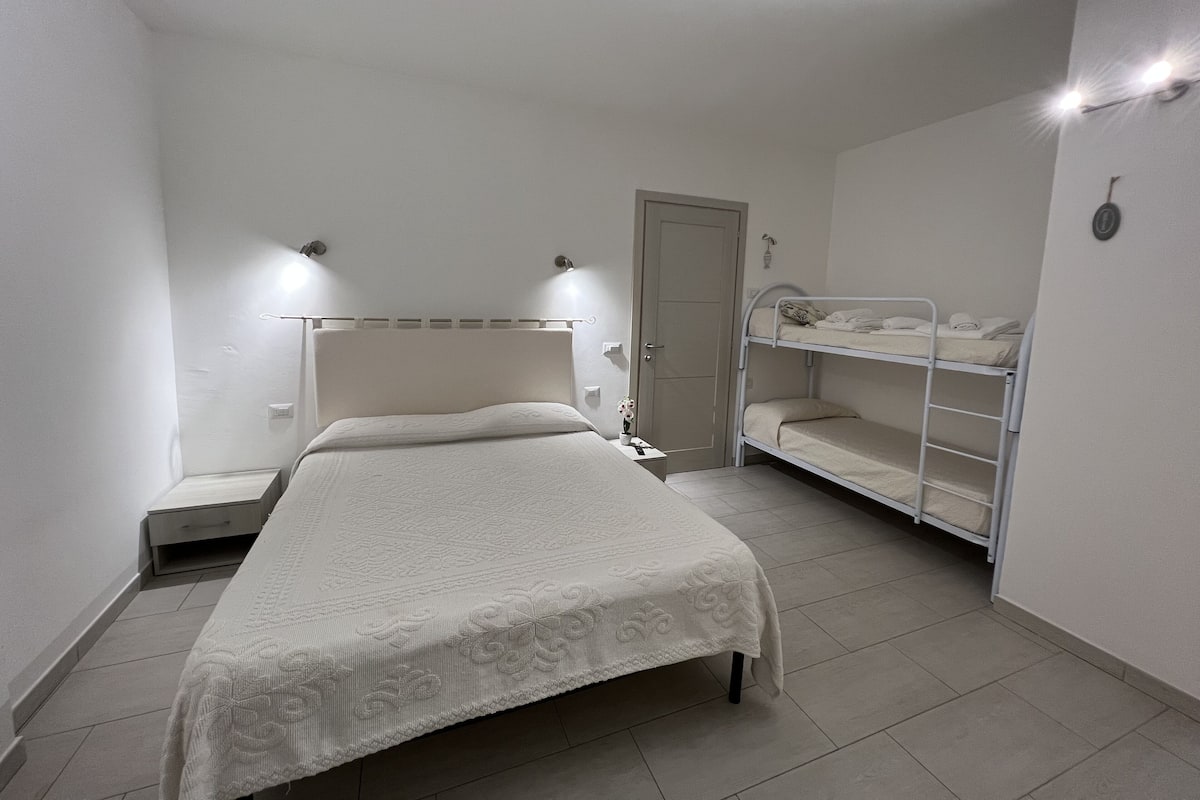 A bedroom with a single bed, a bunk bed, a bedside table, and a door.