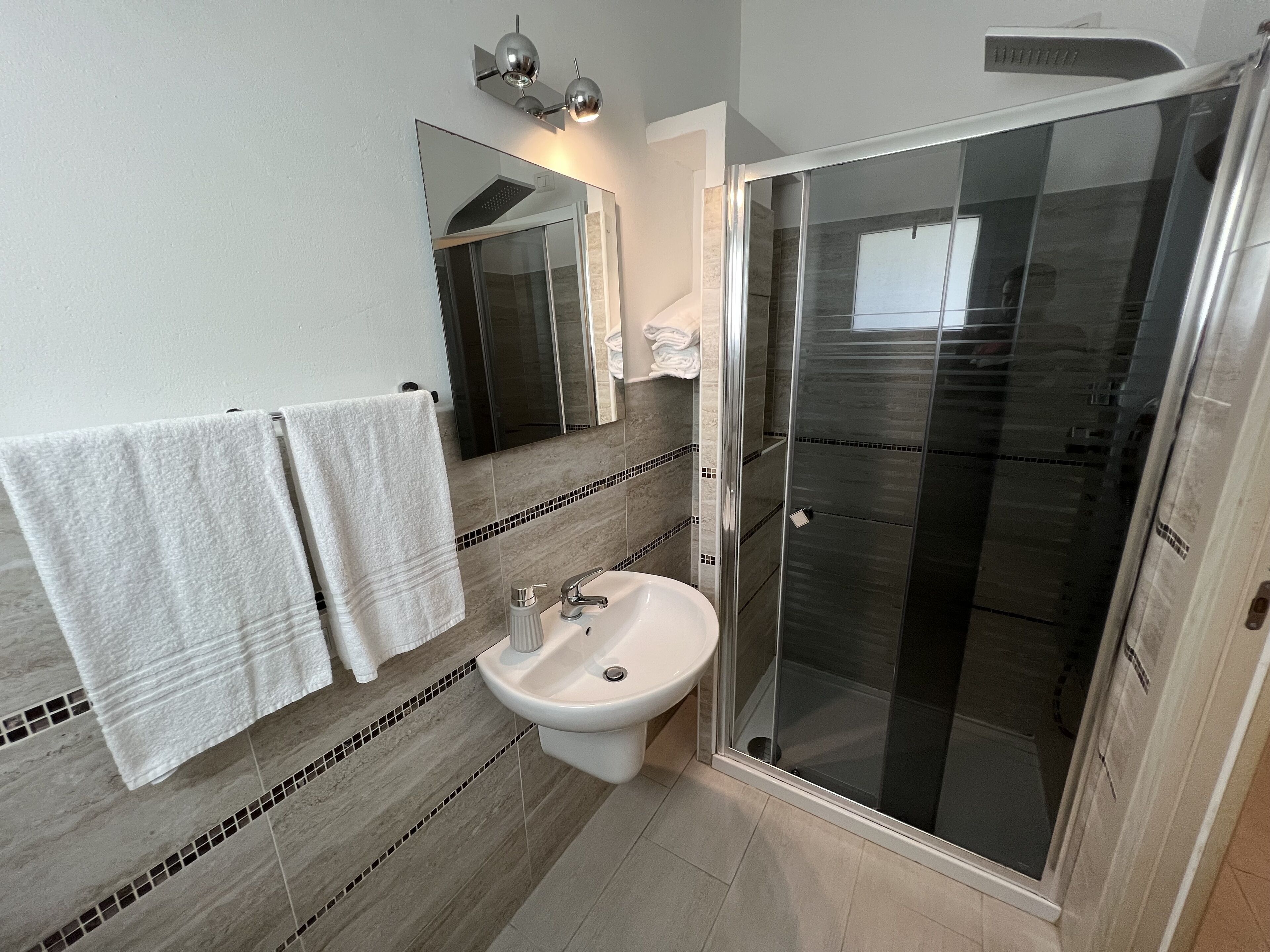 A modern bathroom with a glass shower enclosure, a sink, and two towels hanging on the wall.