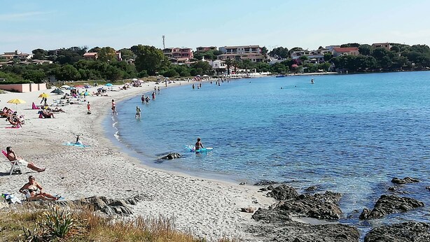 A beach with people sunbathing and swimming, surrounded by buildings and trees. - Al Mare da Francesca (Olbia)