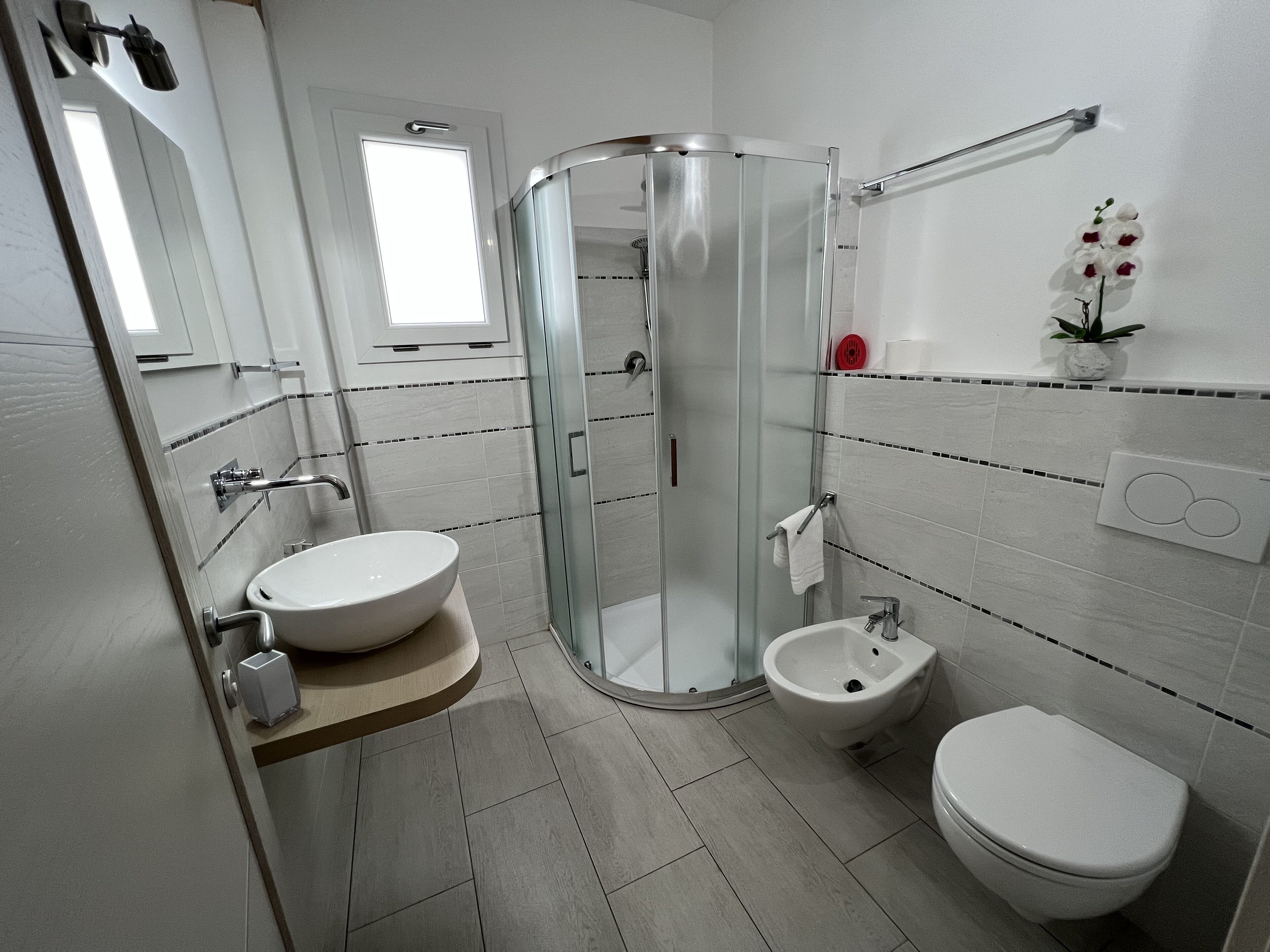 A modern bathroom with a glass-enclosed shower, a sink, a bidet, and a toilet.