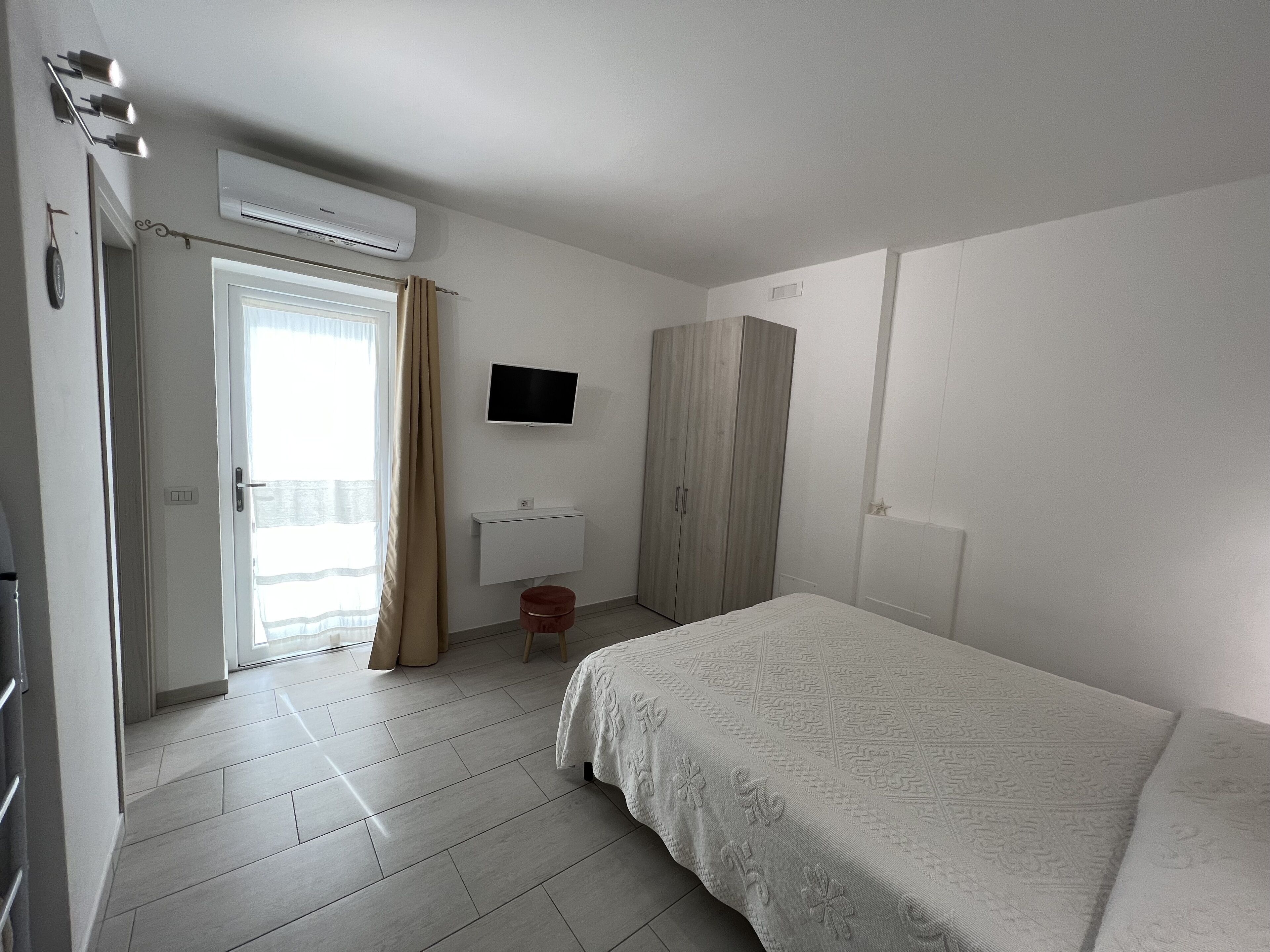 A bedroom with a bed, a wardrobe, a TV, a toilet, and a window with curtains.