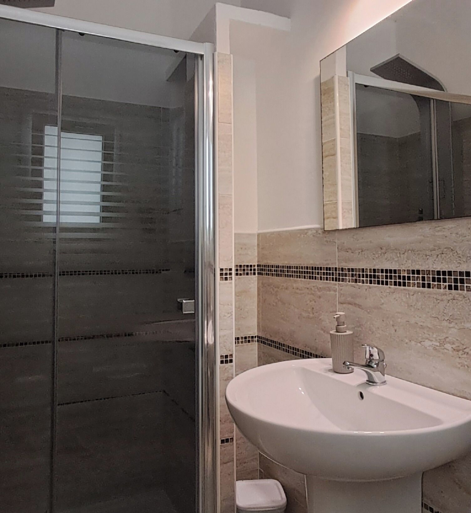 A bathroom with a glass shower door, a white sink, and a mirror above it.