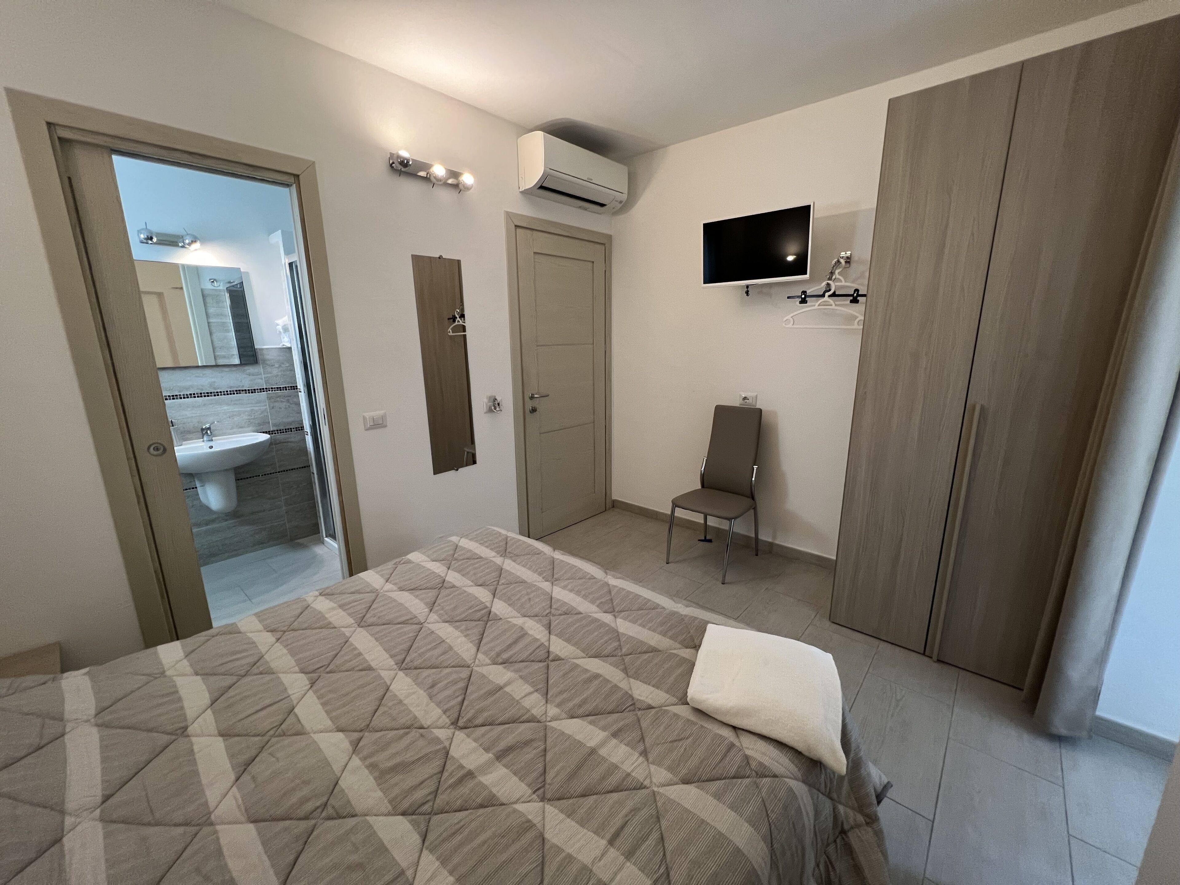 Um quarto com uma cama, uma cadeira, uma TV e um guarda-roupa.