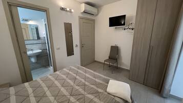Um quarto com uma cama, uma cadeira, uma TV e um guarda-roupa.