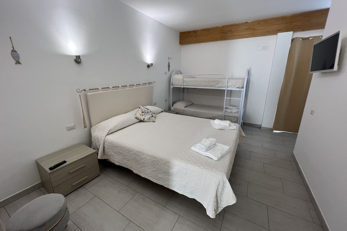 A bedroom with a bunk bed, a bedside table, a small stool, and a TV mounted on the wall.