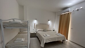 A hotel room with a bunk bed, a single bed, a bedside table with a lamp, and an air conditioning unit. - Al Mare da Francesca (Olbia)