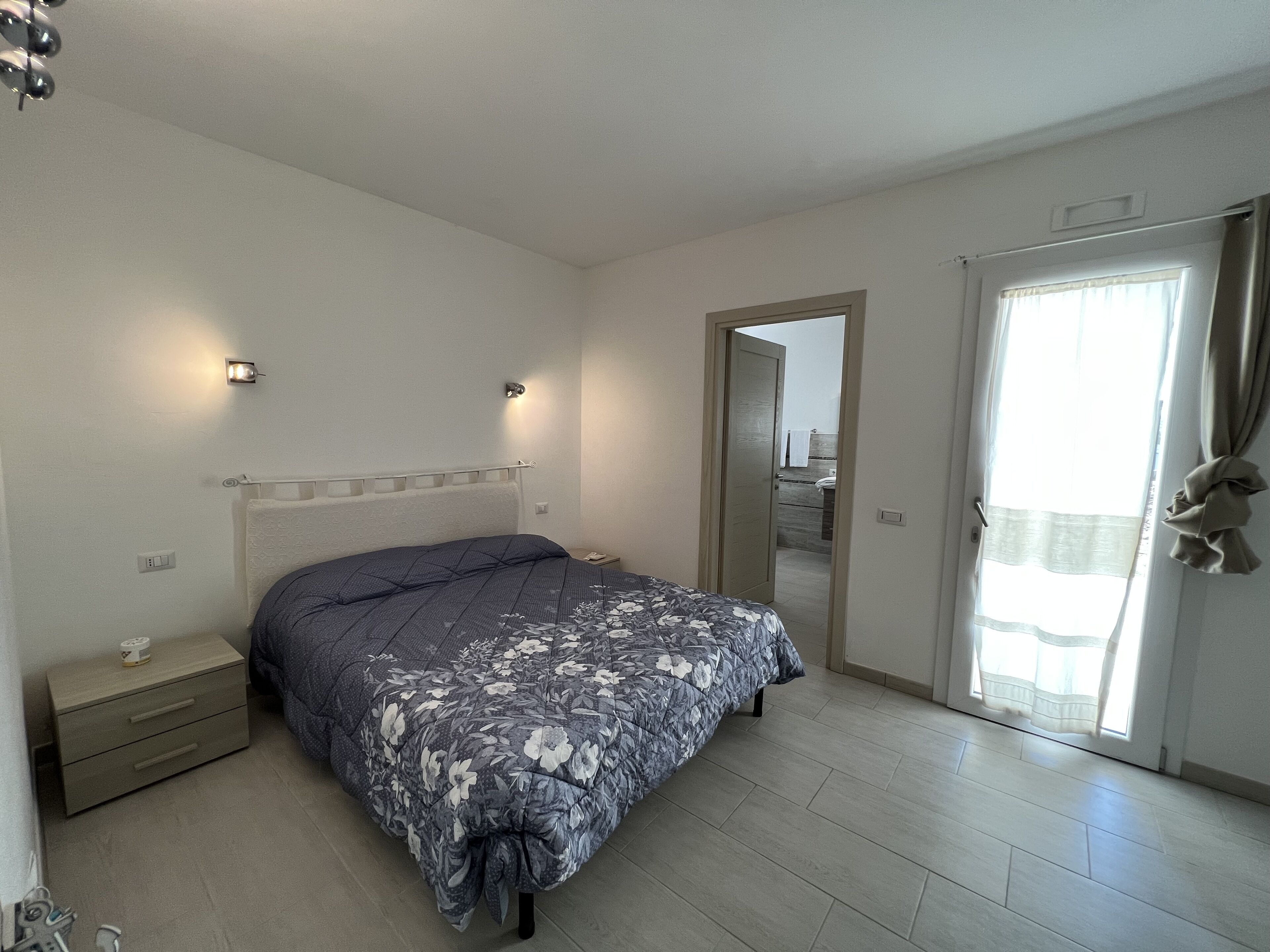 Un dormitorio con cama, mesita de noche y puerta que da a un baño.