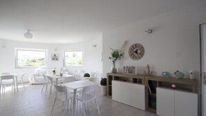 A bright, spacious room with white furniture, large windows, and a wooden cabinet with decorative items. - Al Mare da Francesca (Olbia)