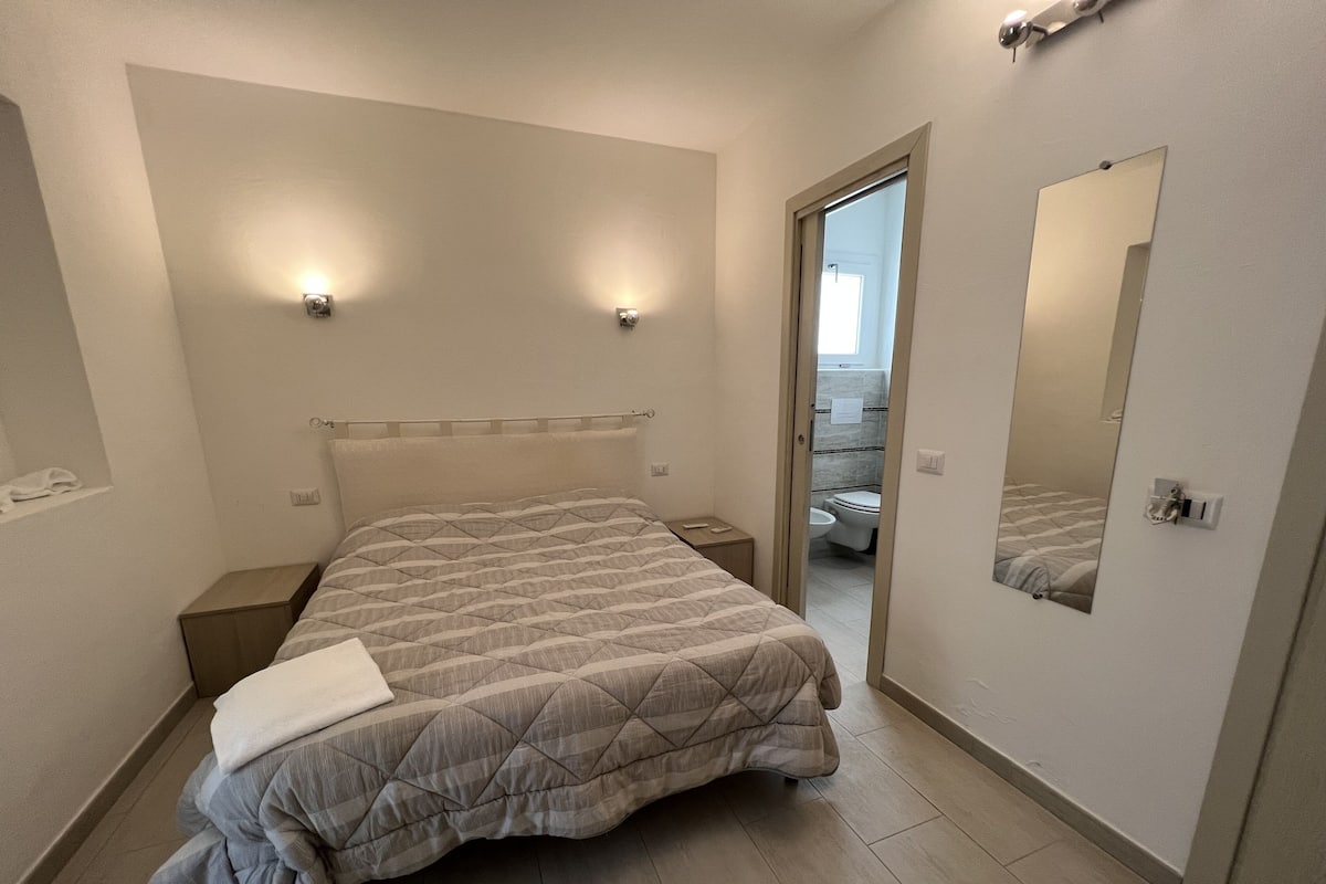 A bedroom with a bed, bedside tables, a mirror, and a door leading to a bathroom.