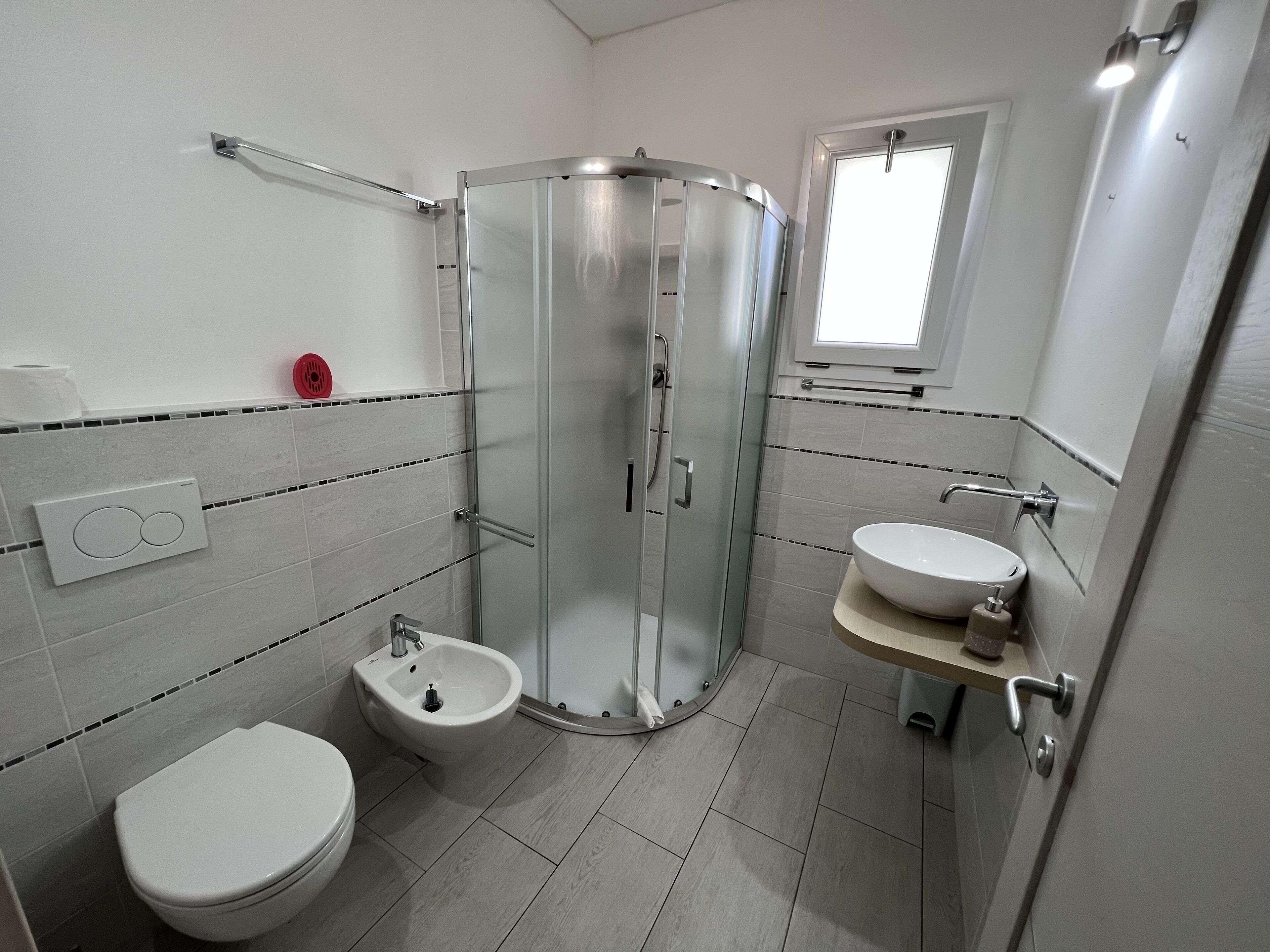 Een moderne badkamer met douche, toilet, toiletbrons en wastafel.