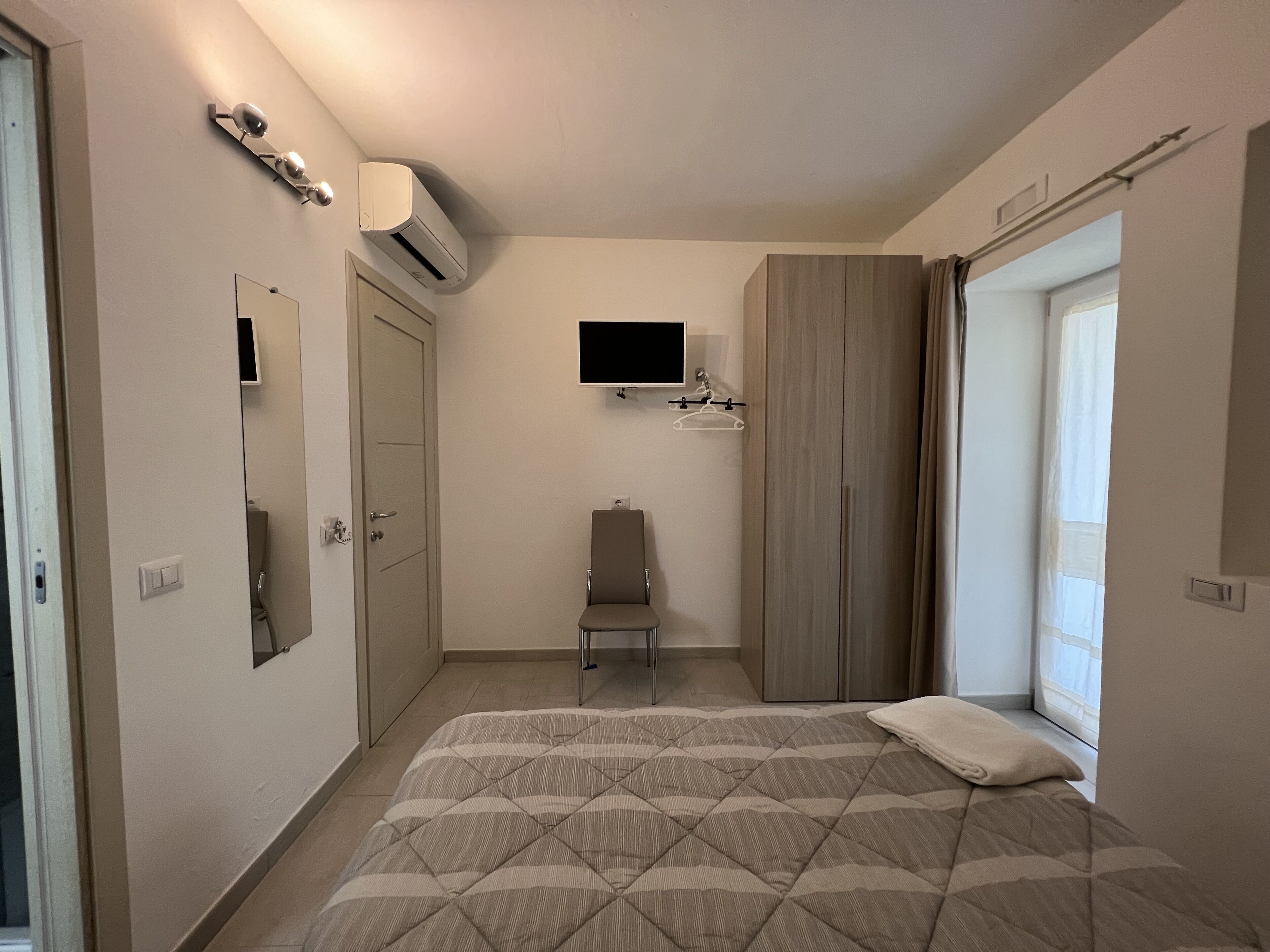 Un dormitorio con cama, una silla, un televisor y un armario.