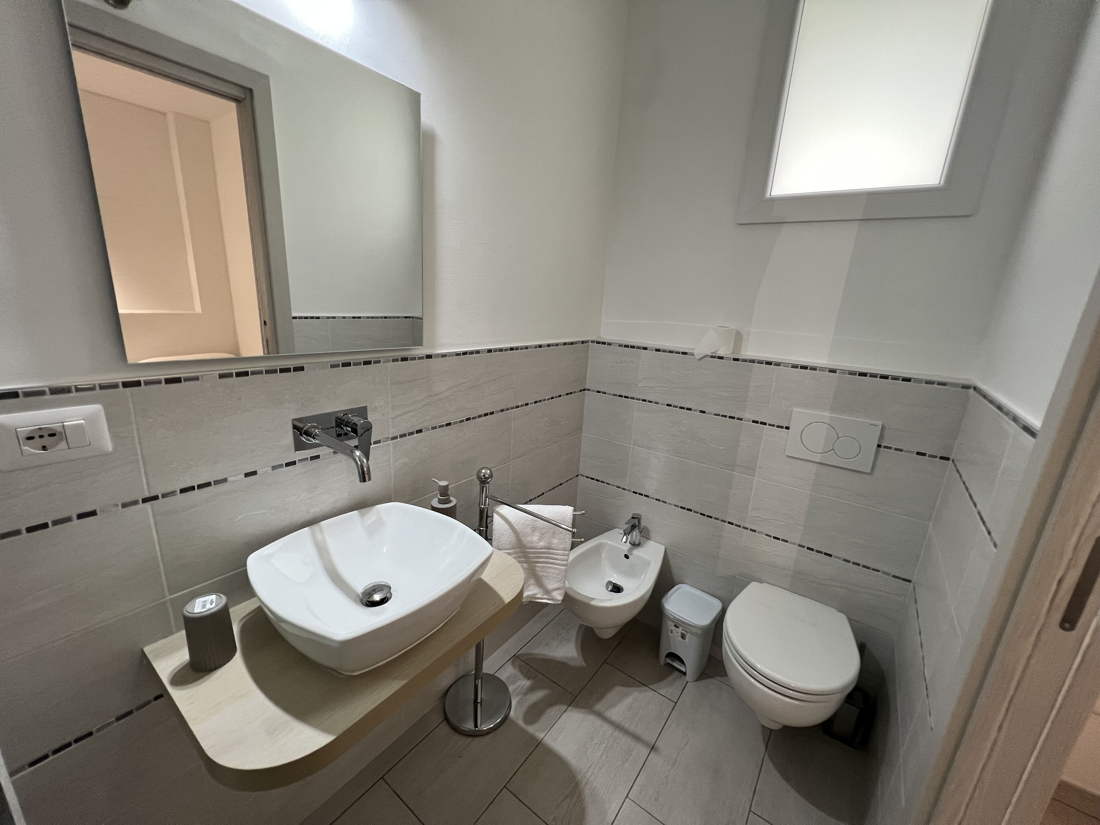 A modern bathroom with a sink, bidet, toilet, and a mirror.
