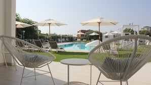 A poolside area with white wicker chairs, a small round table, and umbrellas providing shade. - Al Mare da Francesca (Olbia)