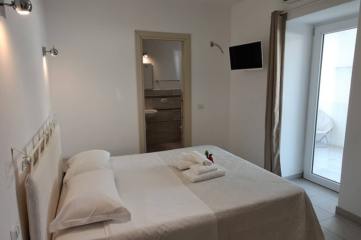 A hotel room with a bed, a TV, a bathroom, and a sliding glass door to the outside.