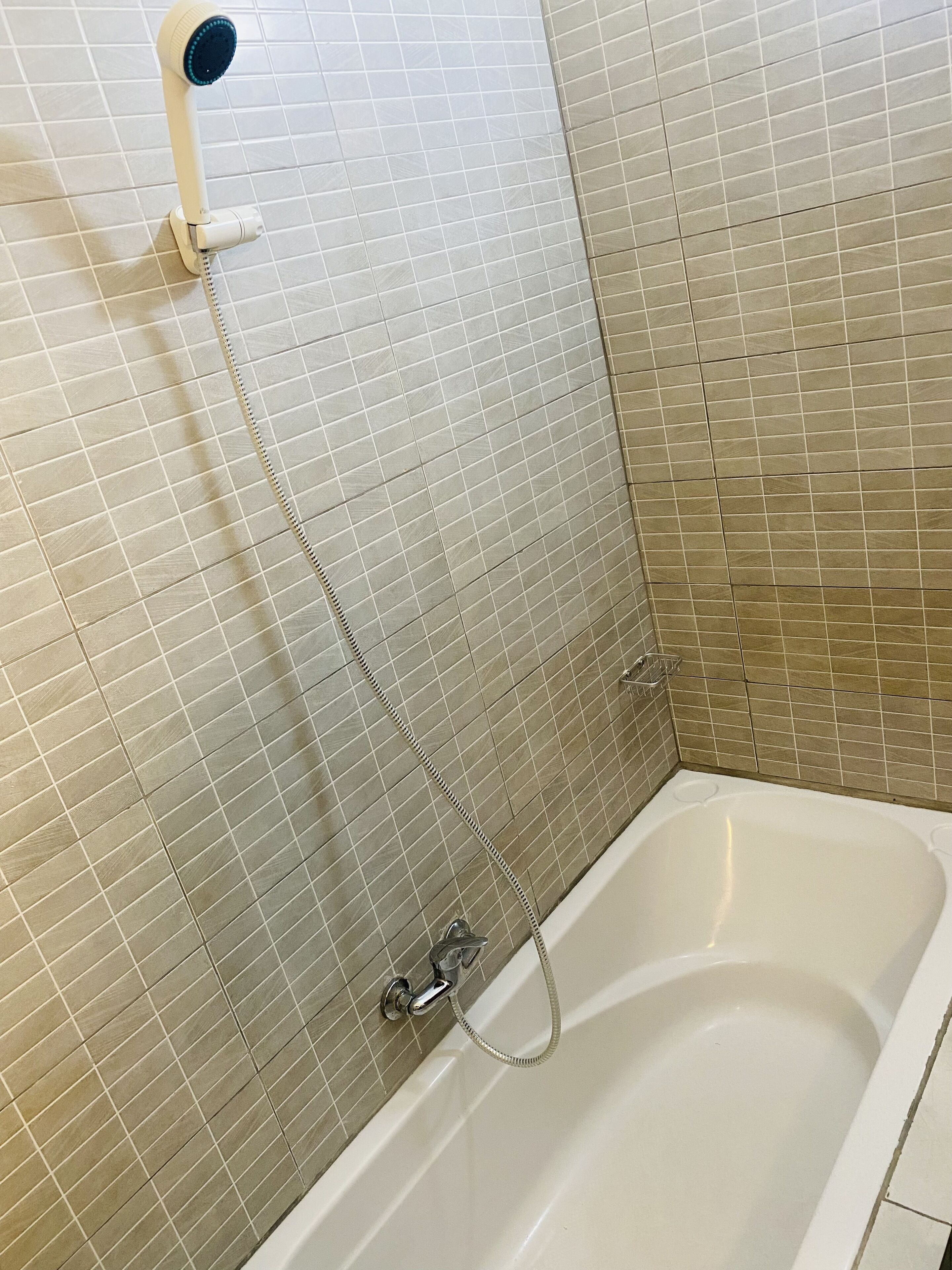 A bathroom with a bathtub, a shower head, and tiled walls.