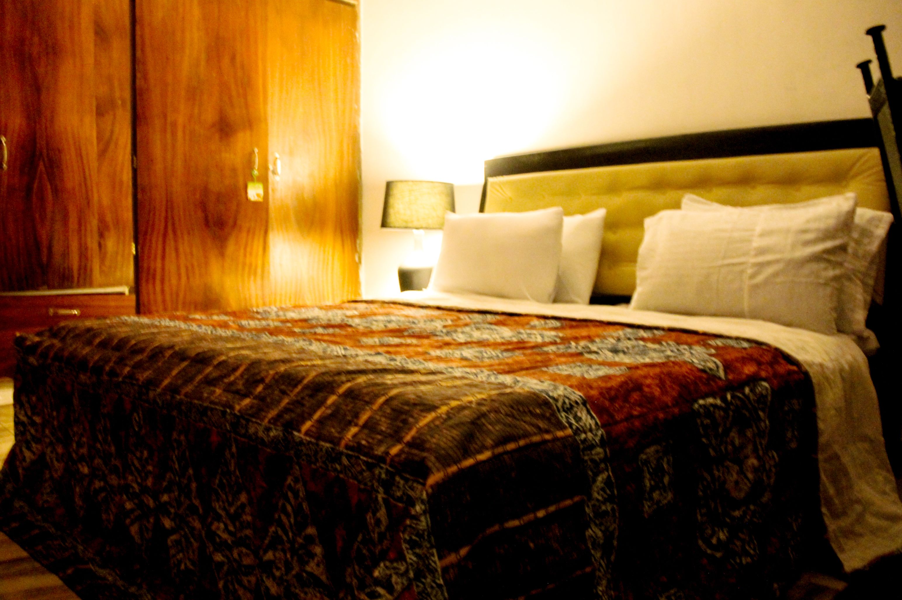 A hotel room with a bed, a wooden wardrobe, and a nightstand with a lamp.