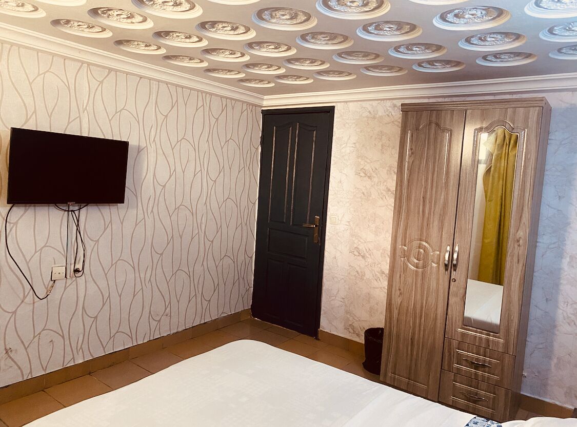 Un dormitorio con cama, armario, televisor montado en la pared y papel tapiz estampado.