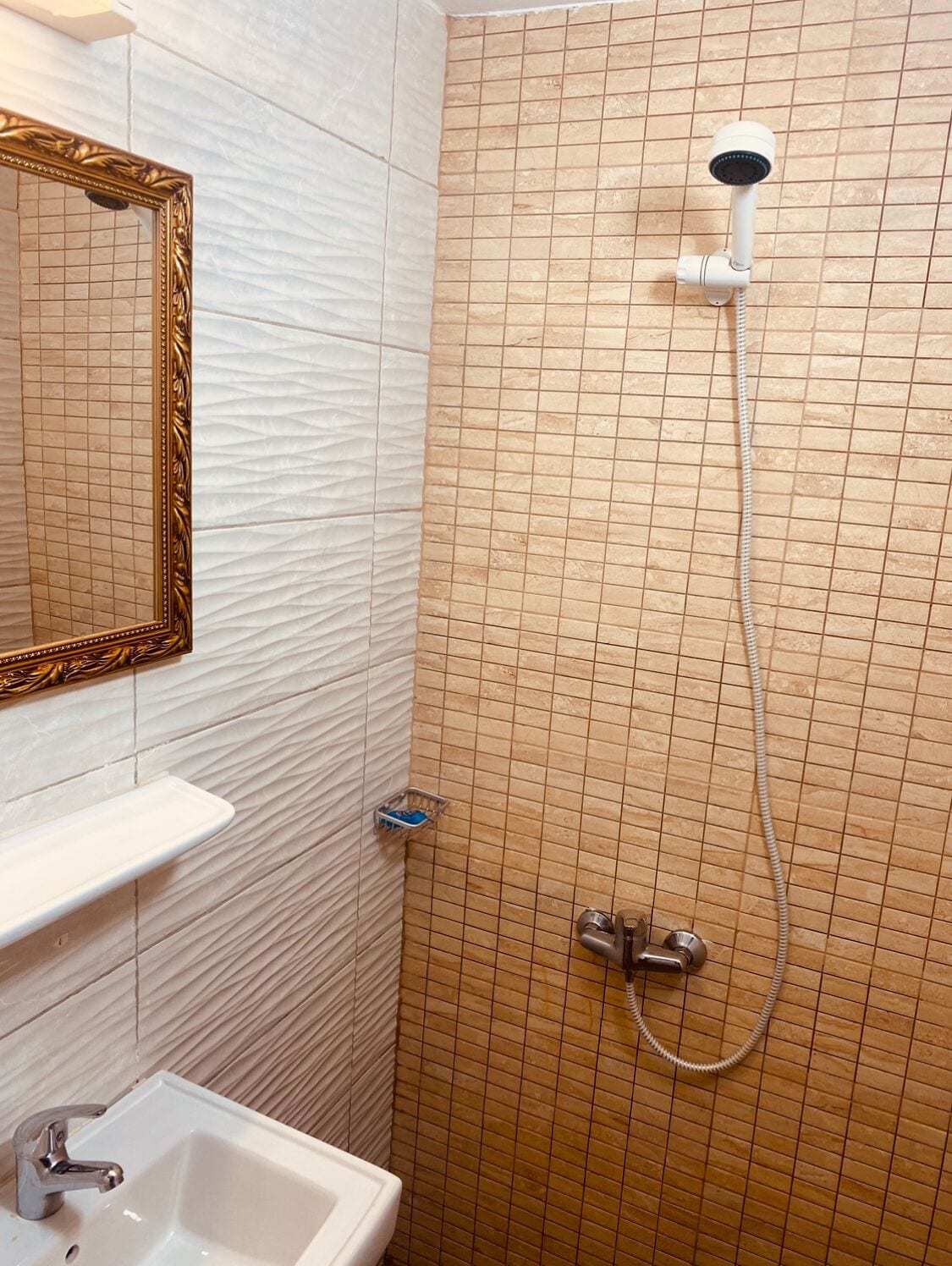 A bathroom with a shower, a sink, and a mirror with a decorative frame.