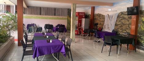 A restaurant with tables covered in purple tablecloths, chairs, and a tiled floor.