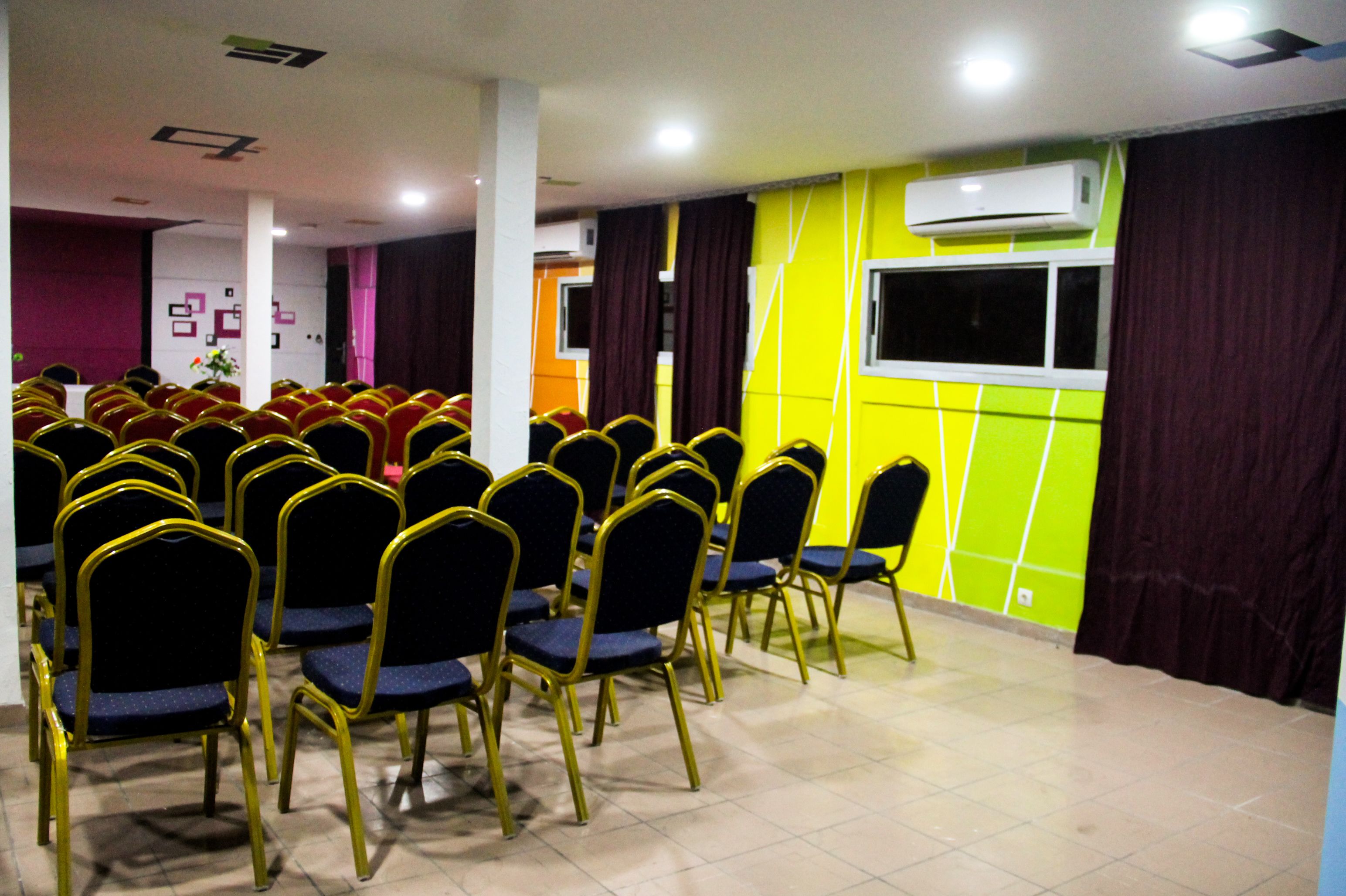 A conference room with rows of chairs, a large window, and an air conditioning unit on the wall.