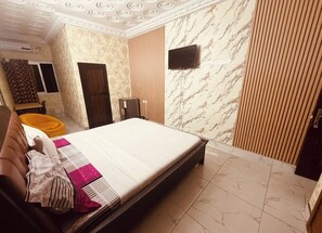 Una habitación de hotel con cama, televisión, puerta de madera y pared con diseño.
