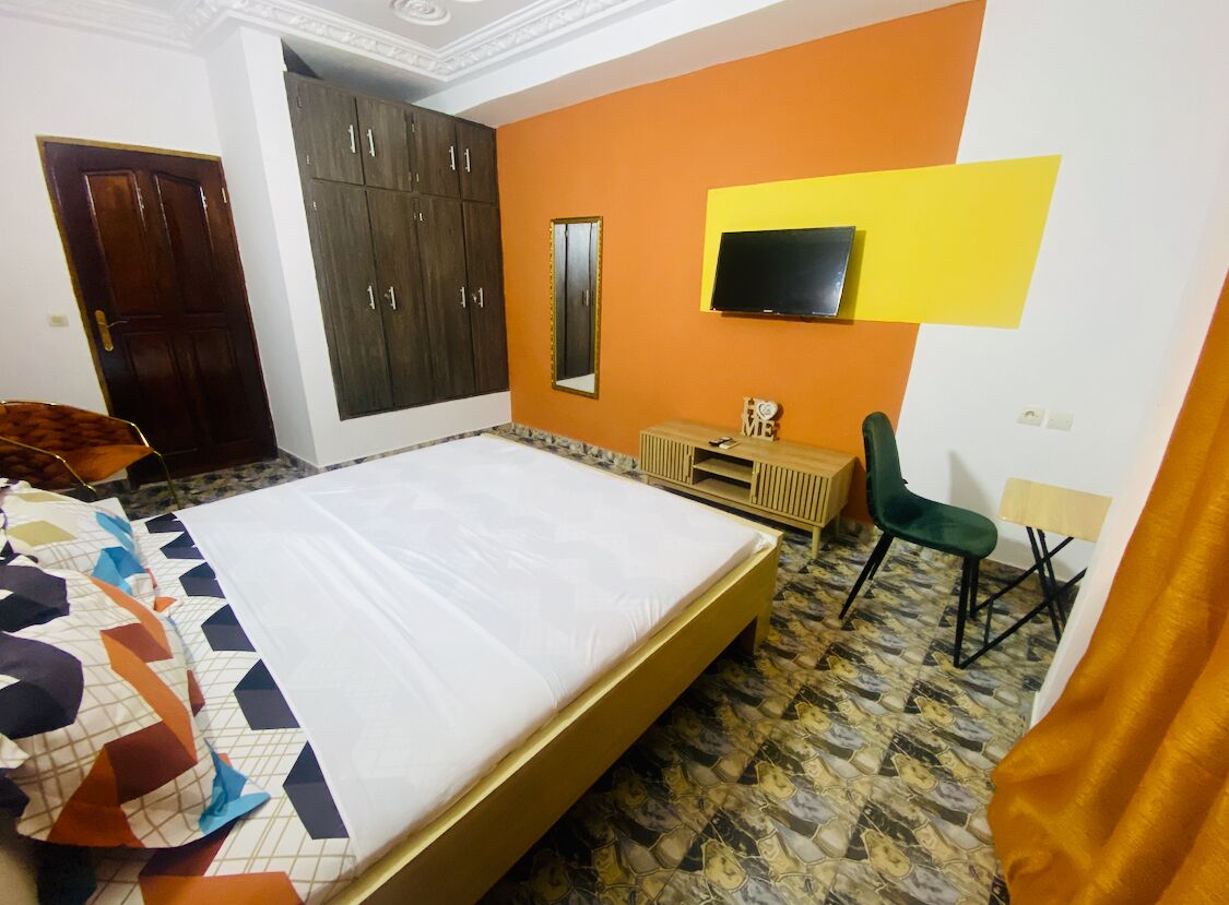 A bedroom with a bed, wardrobe, TV, desk, and chair.