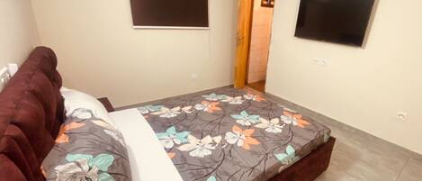 Un dormitorio con cama, televisor de pantalla plana, aire acondicionado y una puerta que da a otra habitación.
