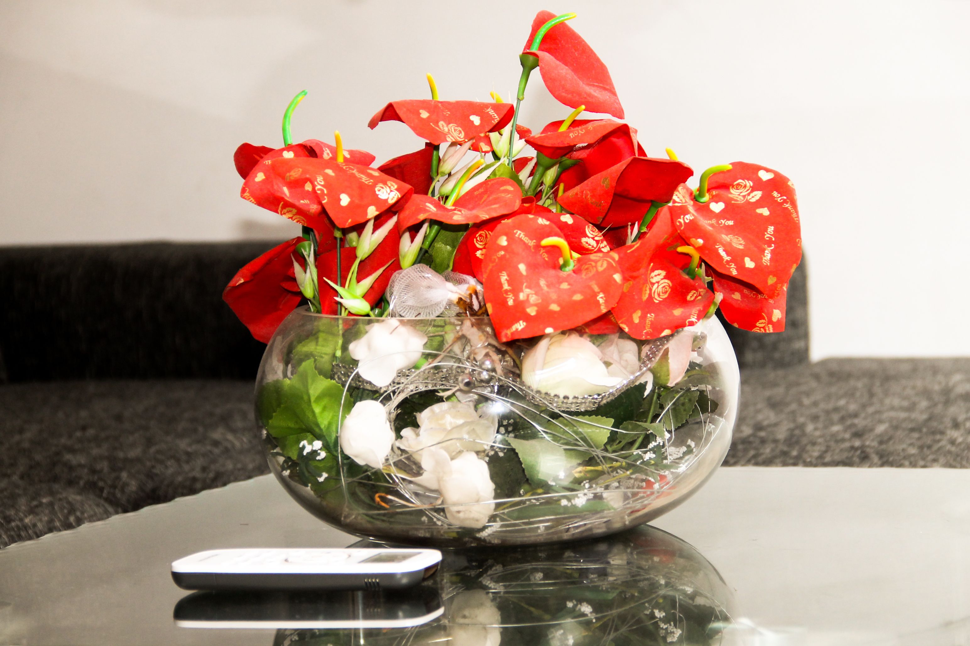 A glass vase with red flowers and decorative elements on a table.