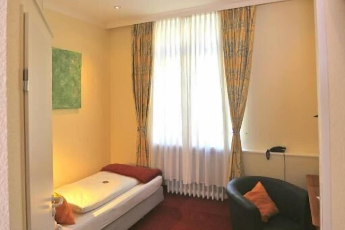 Een kleine kamer met een enkel bed, een stoel, een tafeltje en een radiator.