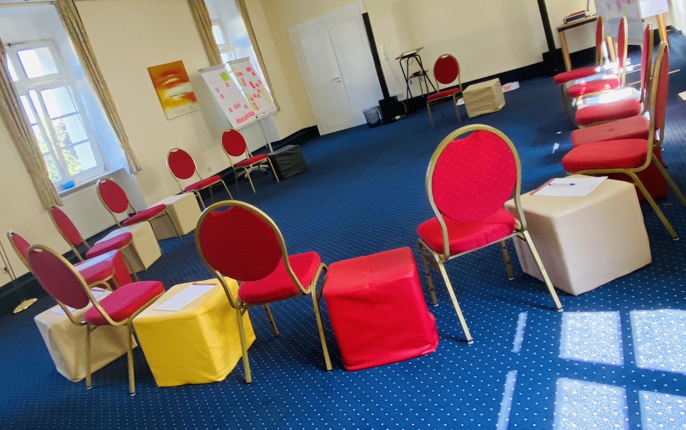 A conference room with rows of red chairs, a whiteboard, and a blue carpet.
