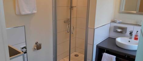 Un baño moderno con ducha de vidrio, inodoro blanco y lavamanos con espejo.