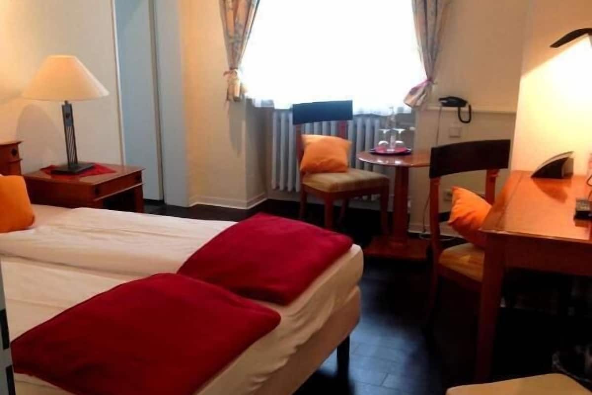 Een hotelkamer met twee bedden, een bureau, een stoel en een klein tafeltje.