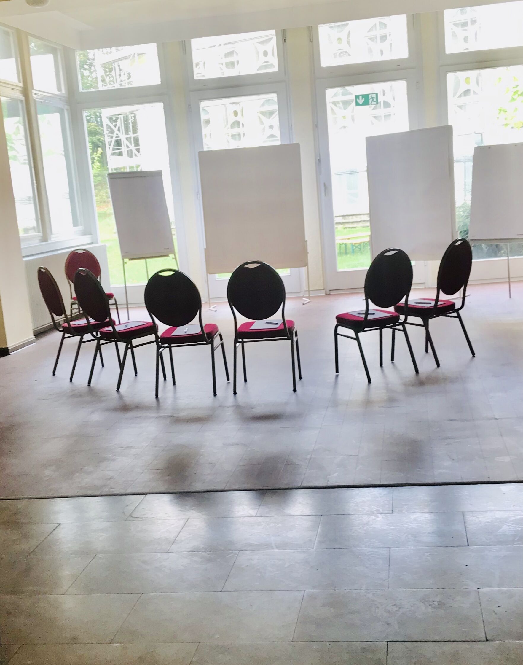 A conference room with six chairs and three whiteboards, large windows, and a tiled floor.